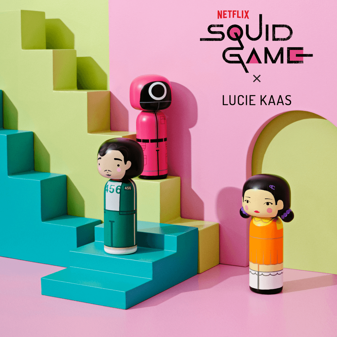 Poupées Kokeshi inspirées des personnages Squid Game sur des marches géométriques colorées.