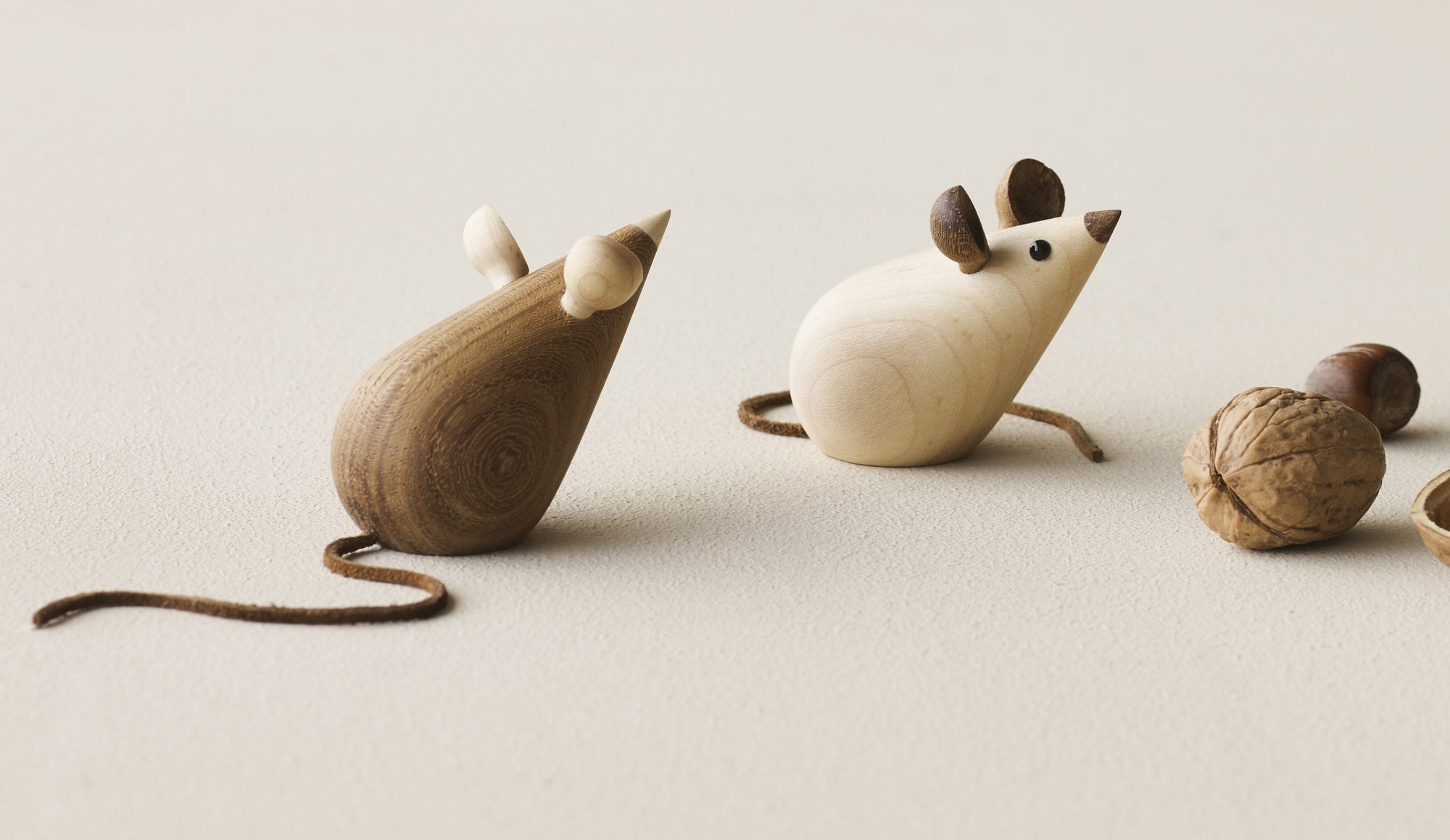 Deux figurines de souris en bois avec de longues queues, à côté de noix sur une surface texturée.
