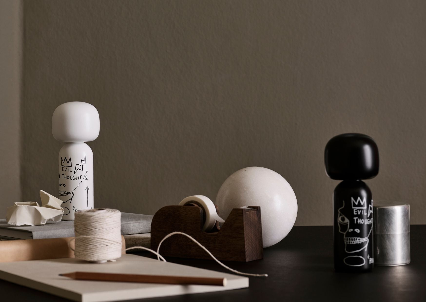 Poupées Kokeshi et divers objets de bureau sur une surface sombre et un fond neutre.