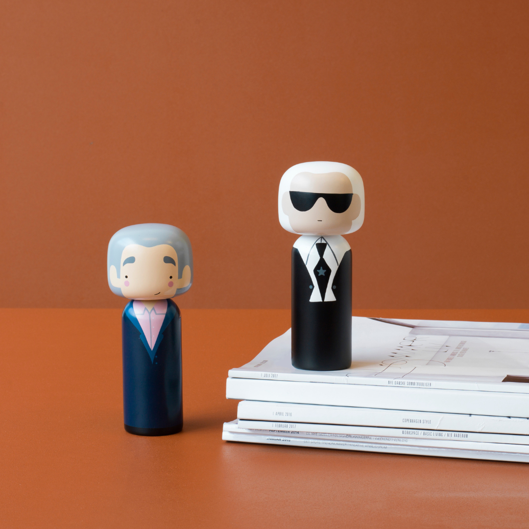 Deux poupées kokeshi sur une pile de magazines sur fond brun.