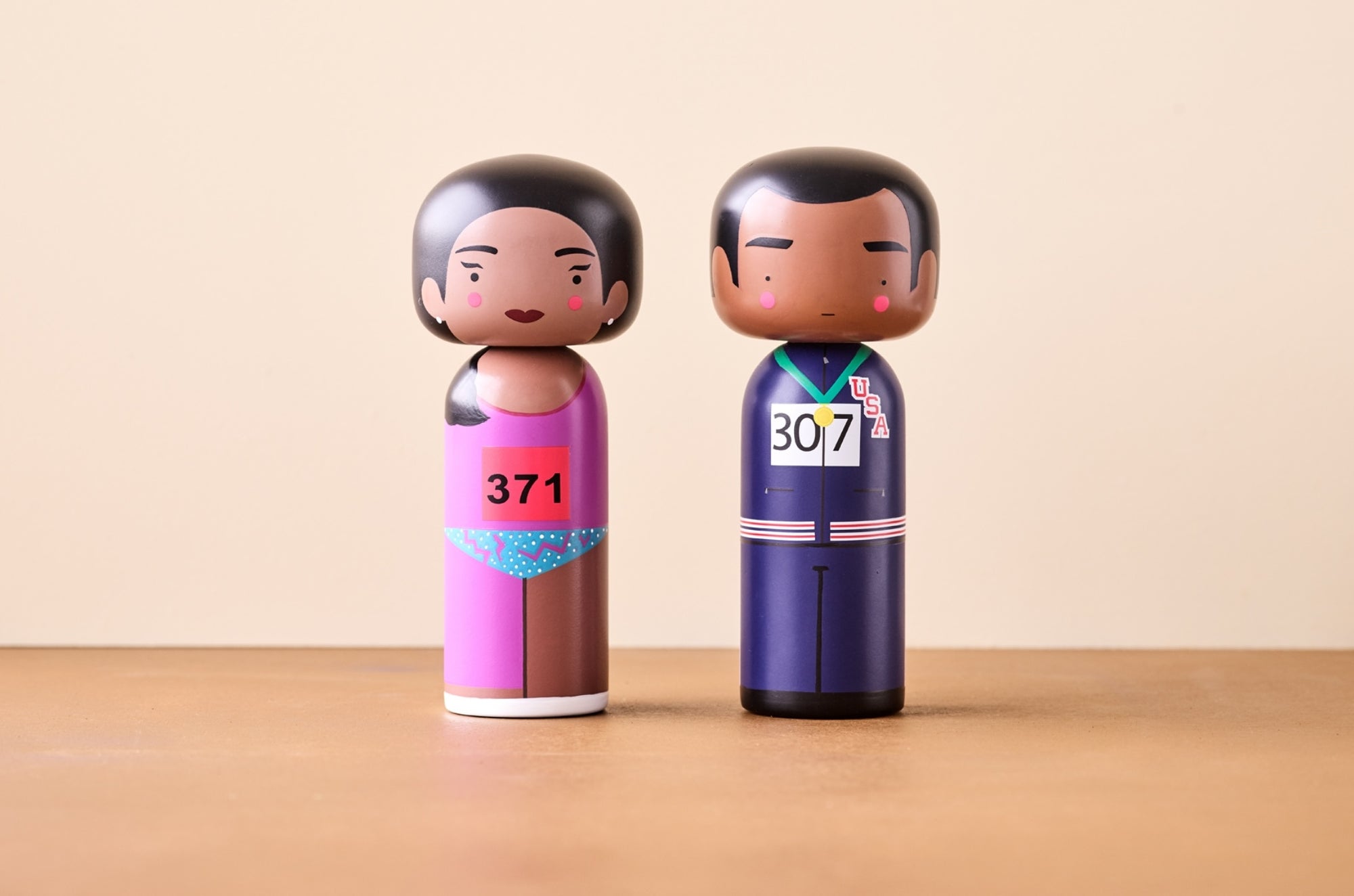 To kokeshi-dukker: en i et rosa antrekk med nummer 371, den andre i et blått antrekk med nummer 307.