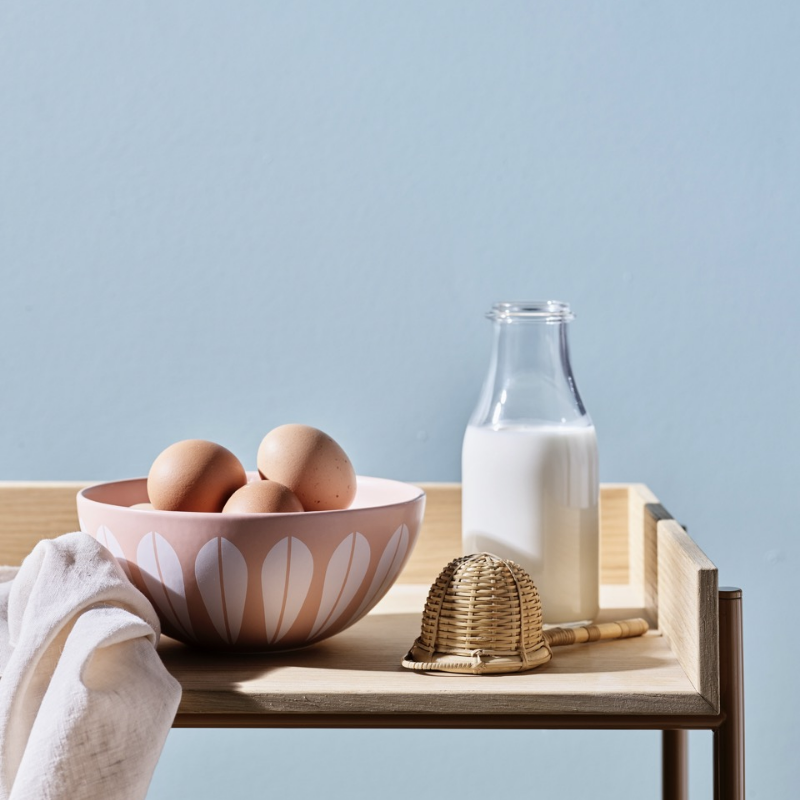 Et trebrett med en rosa bolle med egg, en milk flaske, en honningdypper og en hvit klut.