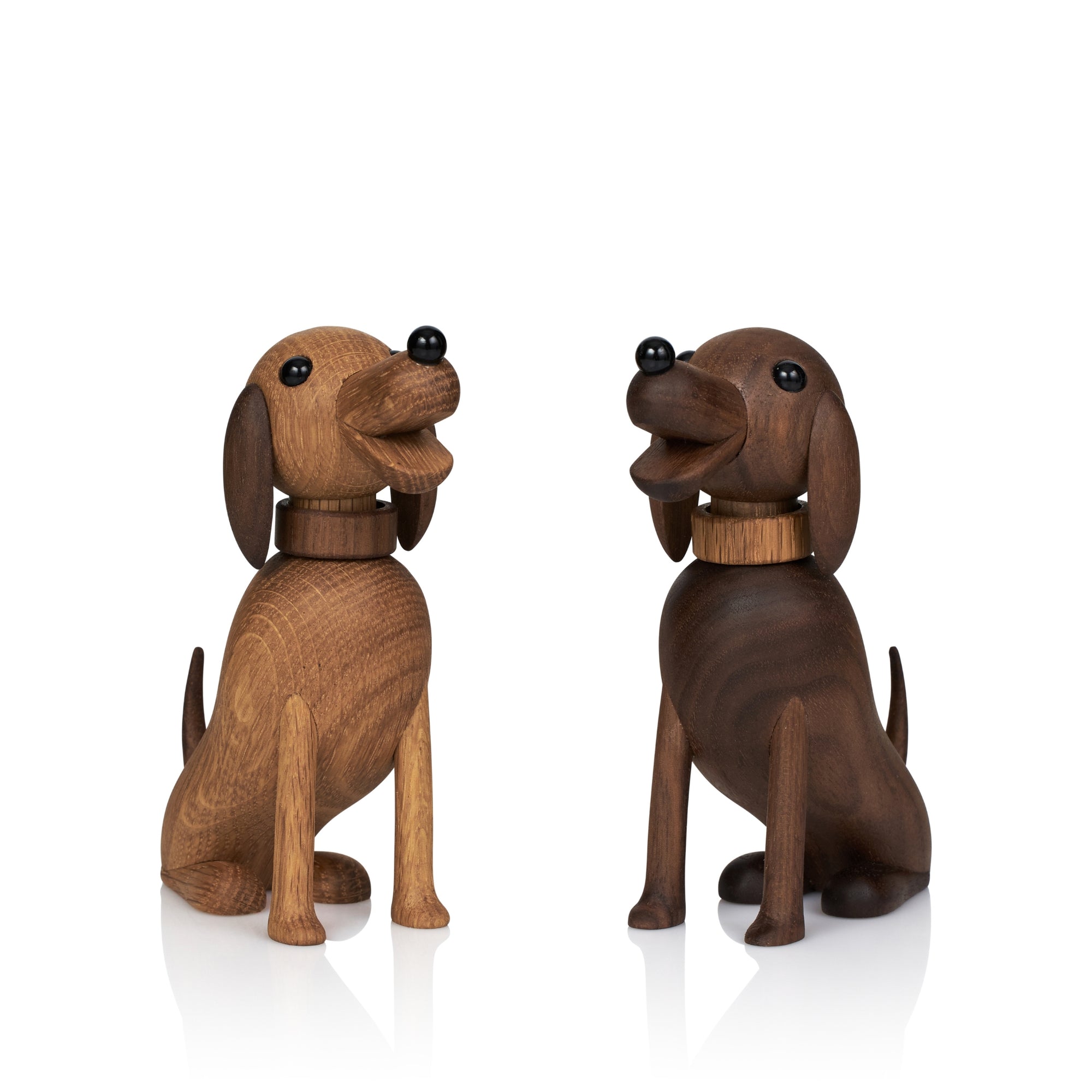 To hundefigurer i tre med halsbånd, en lysebrun og en mørkebrun, sitter side om side.