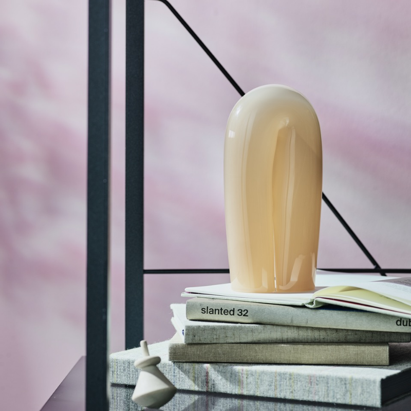 En blank, ferskenfarget keramisk skulptur på stablede bøker med rosa bakgrunn.