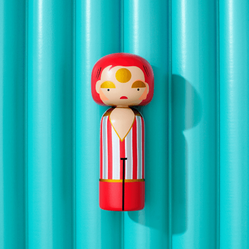 A kokeshi doll with red hair and striped outfit against a turquoise background.