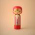 Lucie Kaas wooden kokeshi doll with pink hair, striped red robe and gold facial details