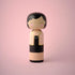 Lucie Kaas kokeshi doll in black dress with pearl necklace and yellow checked jacket on pink background