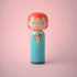 Lucie Kaas kokeshi doll in turquoise suit with red hair and glam‑rock makeup on pink background