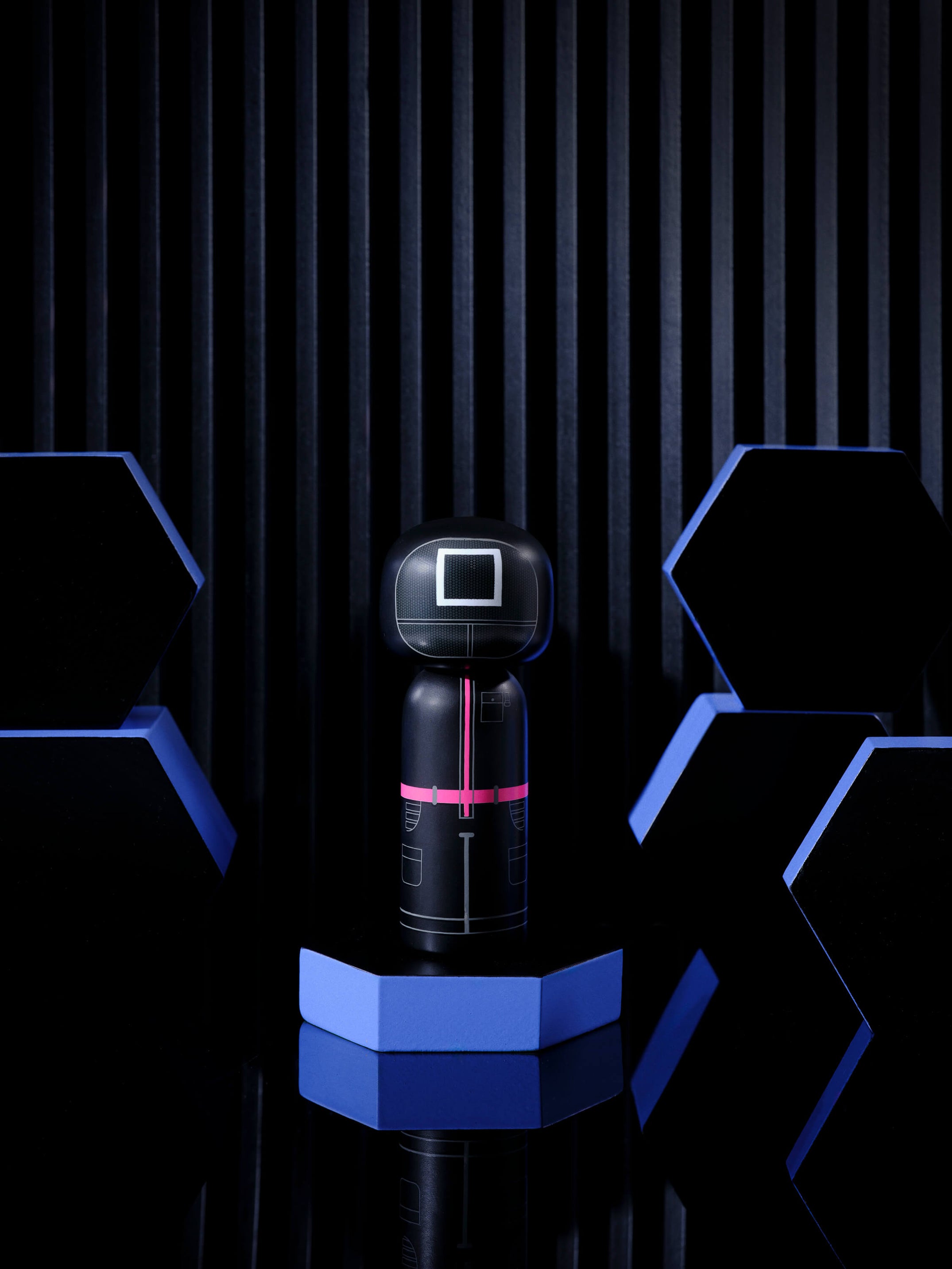 Eine schwarze Kokeshi-Puppe mit rosa und weißen Details auf einer blauen sechseckigen Plattform, umgeben von schwarzen und blauen Sechsecken.