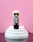 Kokeshi-Puppe mit Sonnenbrille und Anzug auf einem weißen, gestuften Podest vor einem rosa Hintergrund.