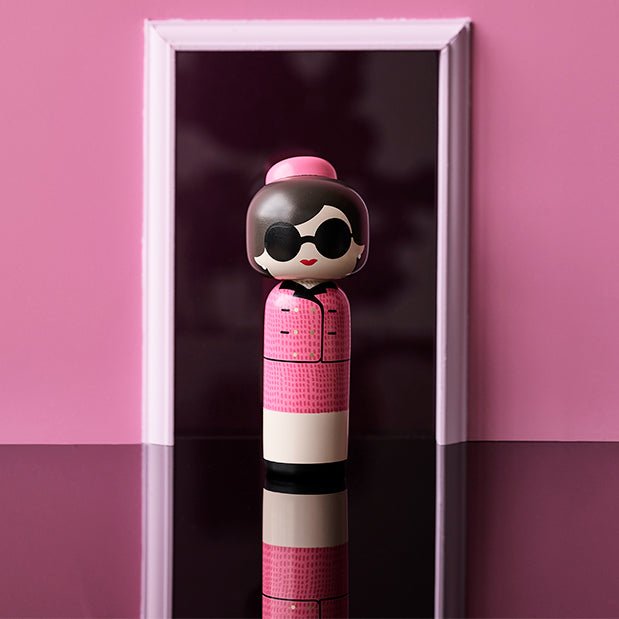 Lucie Kaas' Jackie Kokeshi-Puppe in einem Türrahmen und rosa Hintergrund