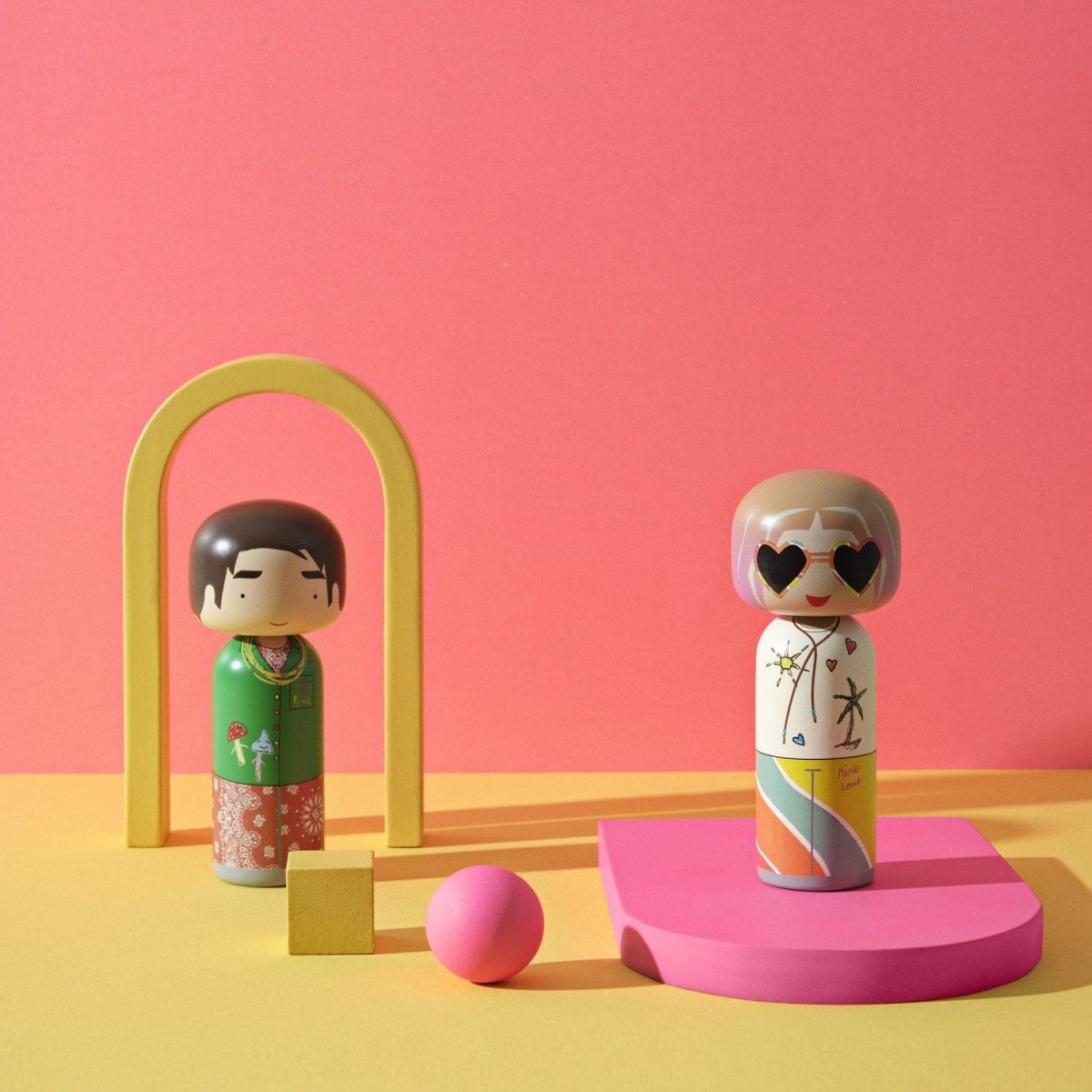 Mira Mikati und Gio Kokeshi-Puppen aus der Mira Mikati-Kollektion von Lucie Kaas in einem orangefarbenen Rahmen mit rosa Verzierungen