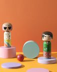 Mira Mikati und Gio Lucie Kaas Kokeshi-Puppen aus der Mira Mikati-Kollektion in einem orangefarbenen Rahmen mit Dekorationen
