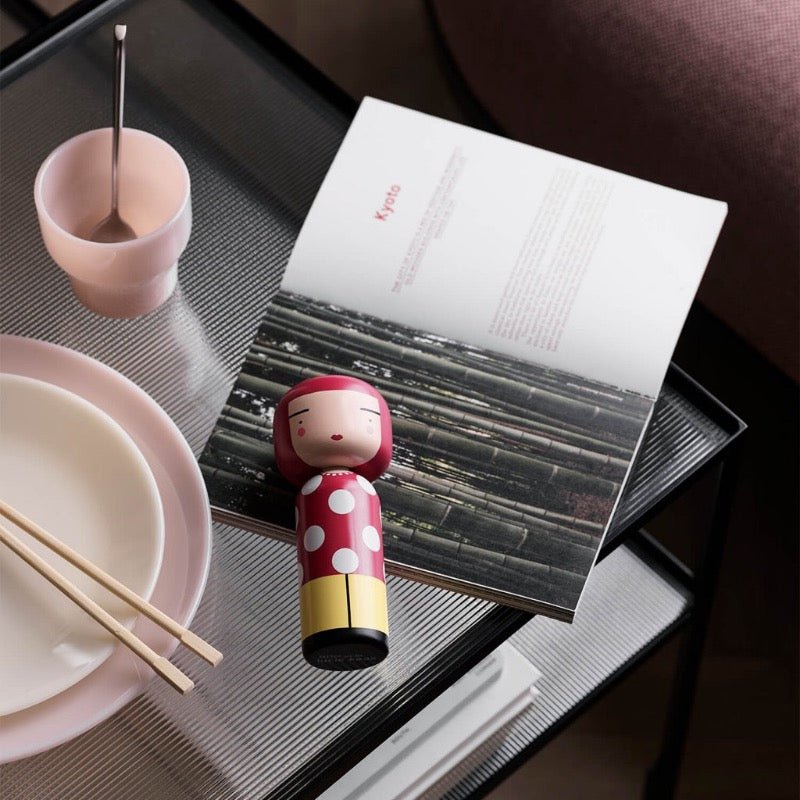 Kokeshi de Lucie Kaas Dot sur une table avec un magazine et de la vaisselle