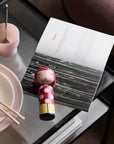 Kokeshi de Lucie Kaas Dot sur une table avec un magazine et de la vaisselle